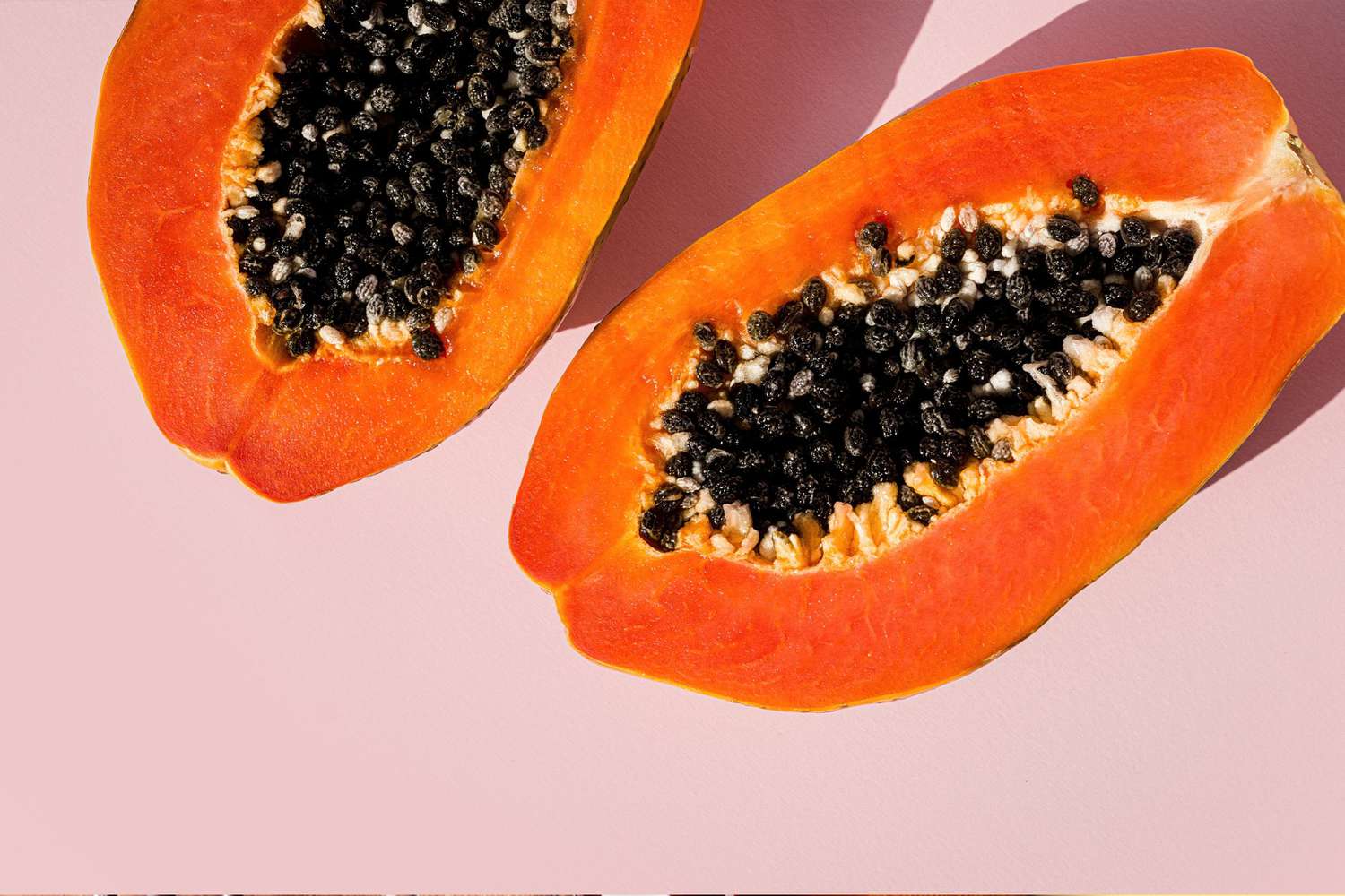 Papaya health benefits and nutrition: ripe papaya cross-section on a pink background