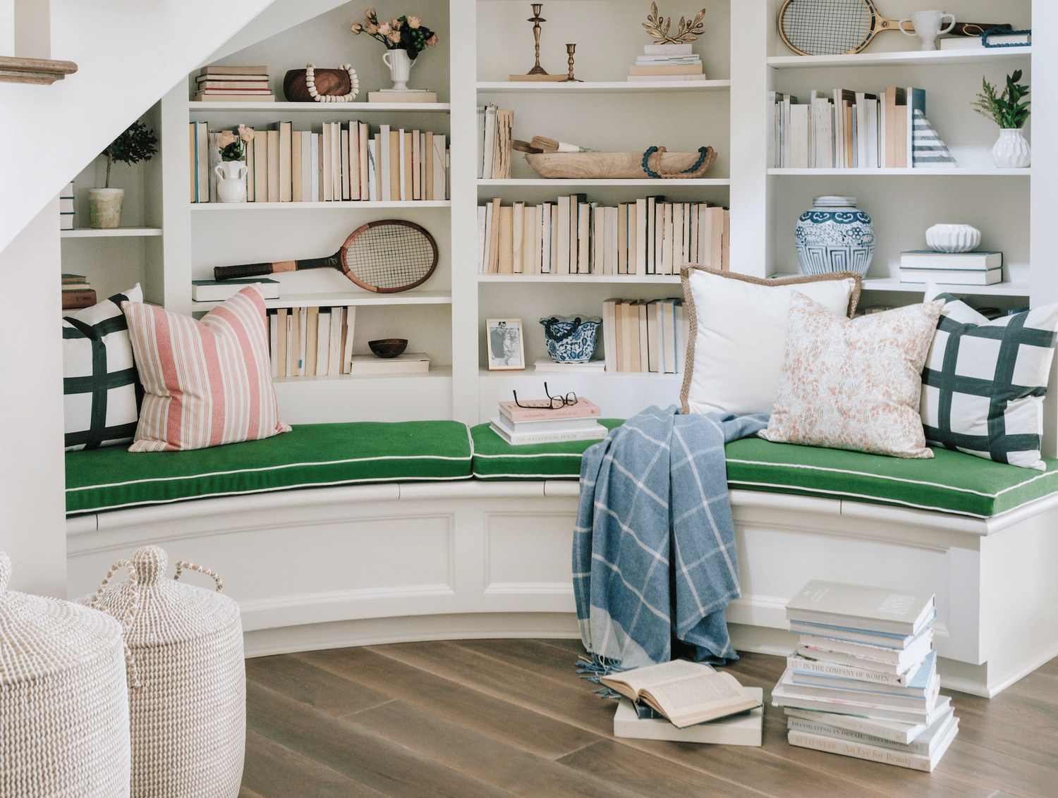 Reading nook under stairs with green cushion and pink pillows and bookcases