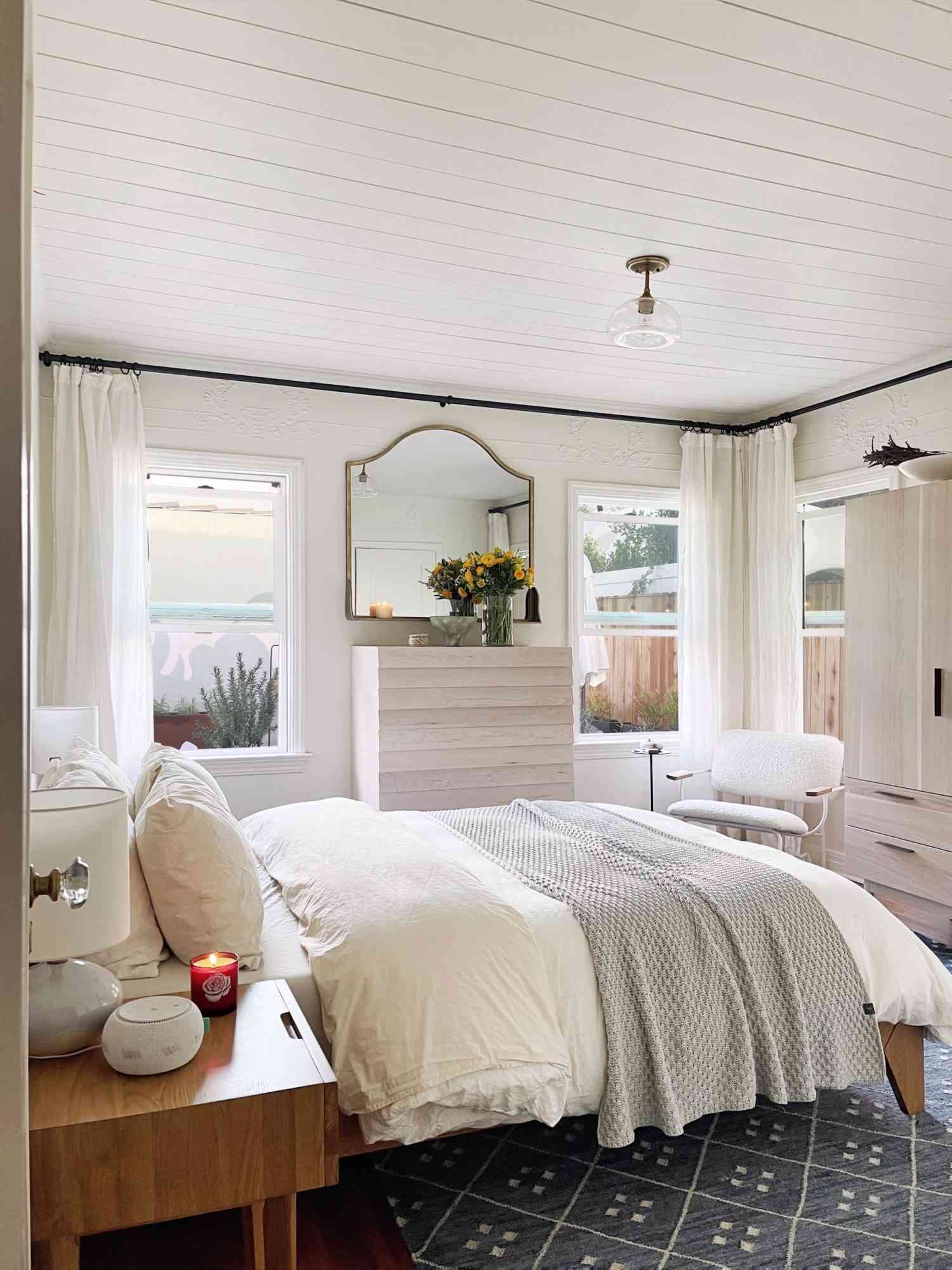 Bedroom with neutral bedding, white curtains, and shiplap ceiling