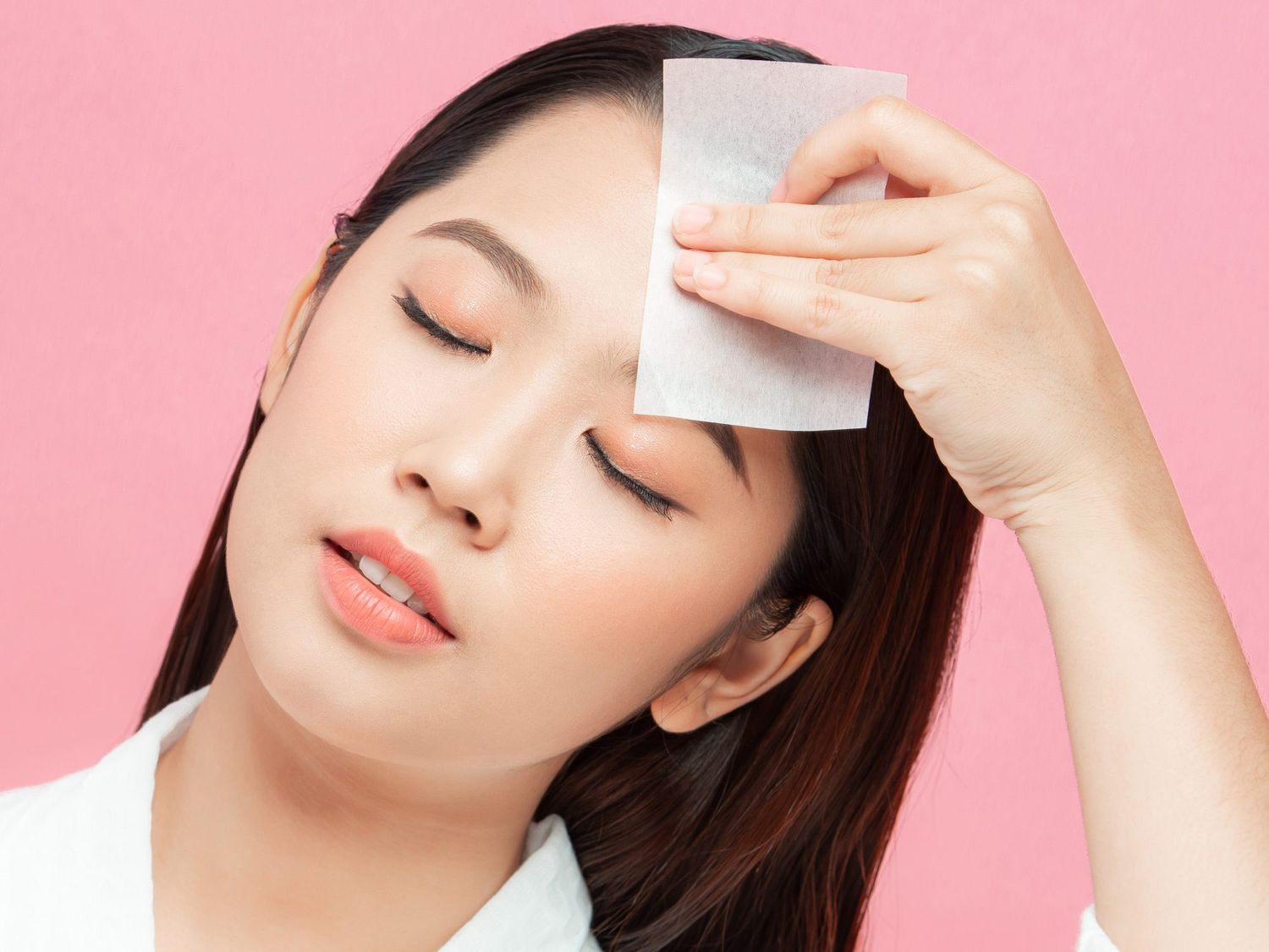 Woman using facial oil blotting paper. Photo of woman with perfect makeup on pink background. Beauty concept