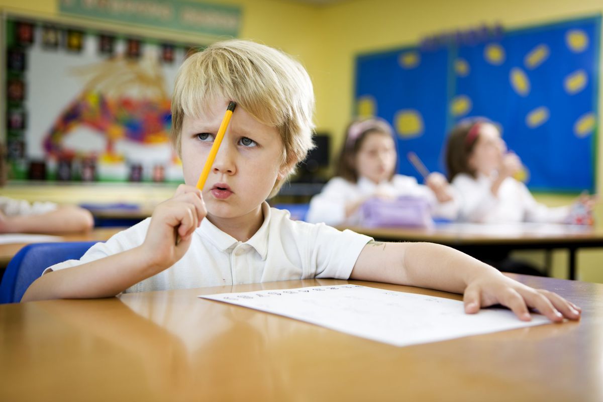 Little Boy Sitting at School Desk with Pencil