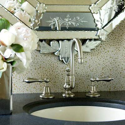 a close up view of a classic bathroom faucet with a decorative patterned mirror behind it and dark countertop