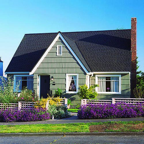 purple flowers line the front of a white fence with yellow flowers lining the front of the house