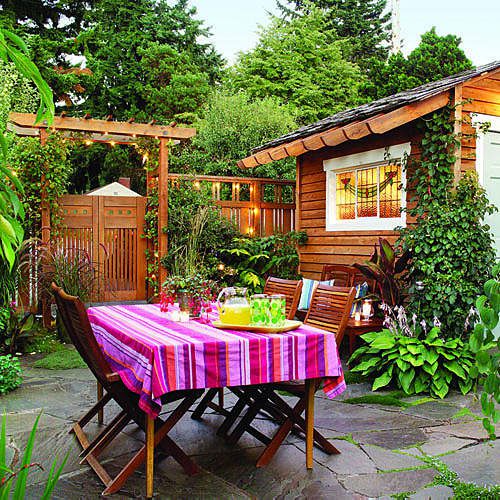bright and colorful backyard with a striped tablecloth over an outdoor table with a wooden garden shed, in the background