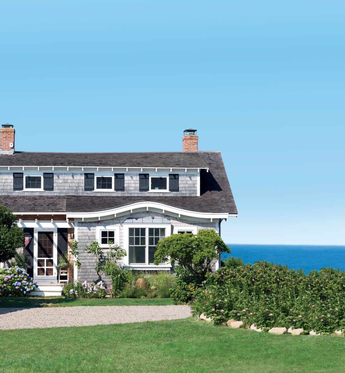 Cape Cod-style beach cottage in Orleans, Massachusettes with gray shingles, black shutters, and a water view.
