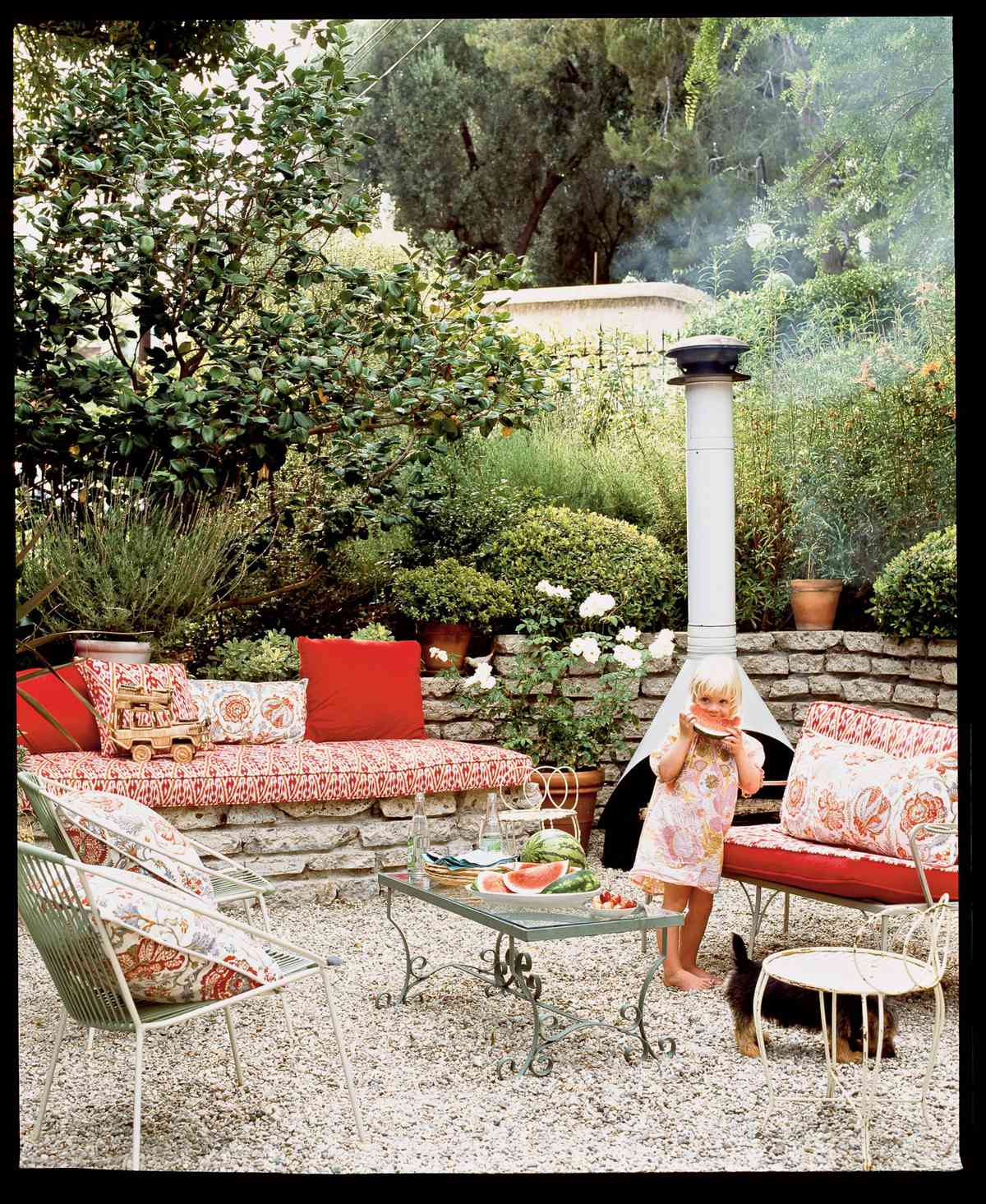 <p>Bright red throw pillows and patterned fabrics bring this outdoor space to life. A low stone wall creates a natural barrier around the living space, and pebbles replace grass underfoot for a low-maintenance ground covering.</p>
                            