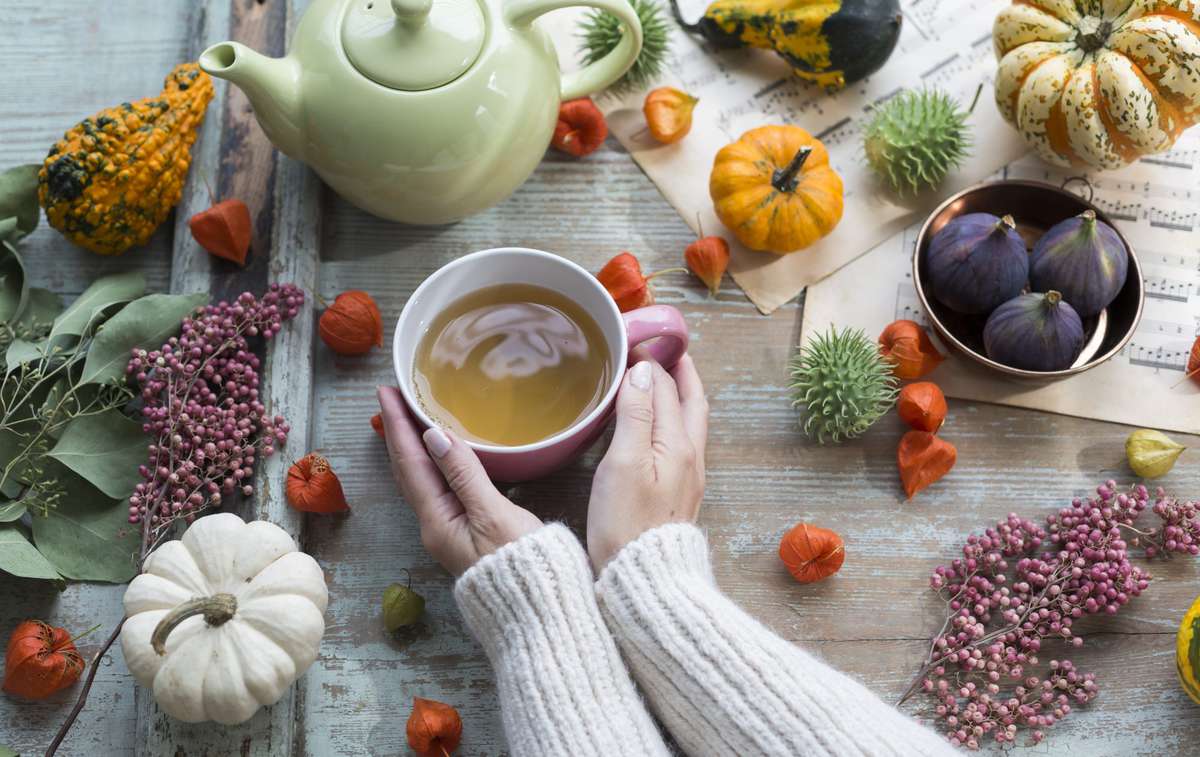 Woman warming her hands on cup of tea in autumn