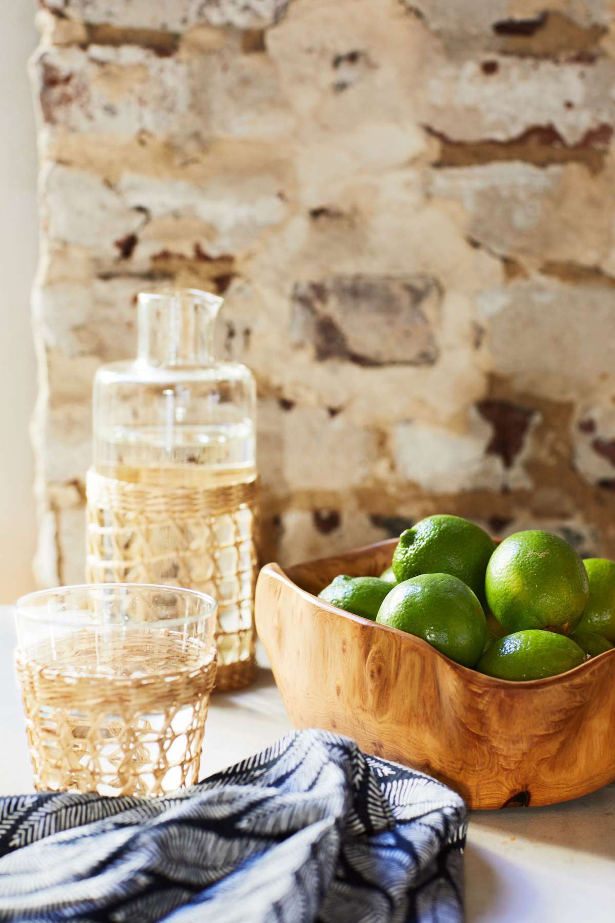 Bowl of limes and water glasses on counter against brick wall
