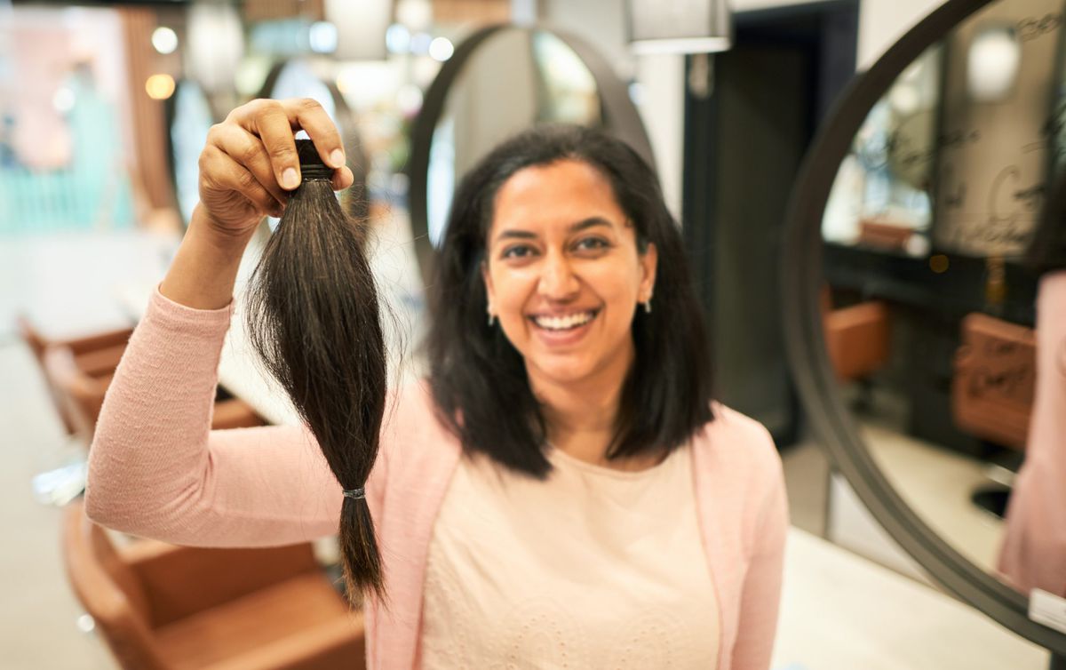 Smiling young woman holding up her cut ponytail in a salon