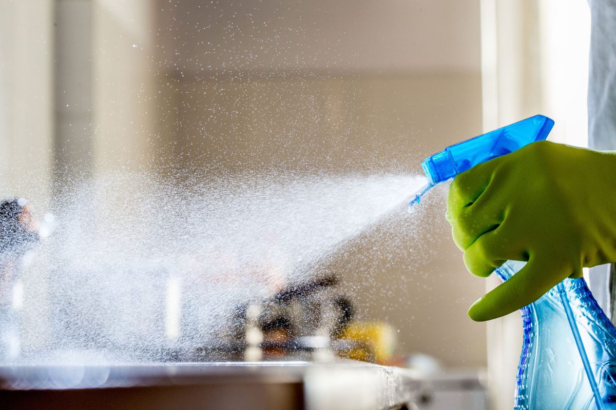 Gloved Hand Spraying the Kitchen Counter with Cleaner
