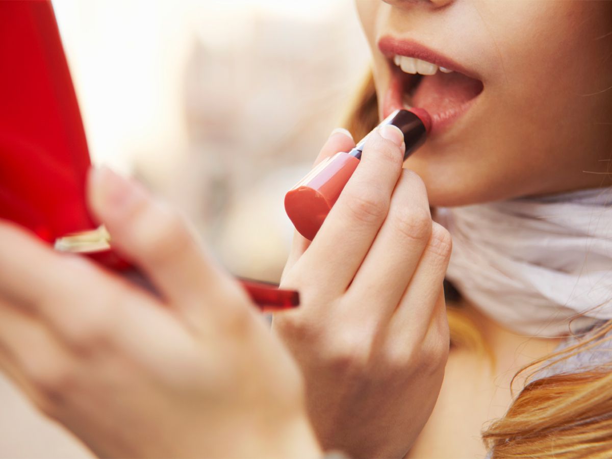 young woman putting on lipstick
