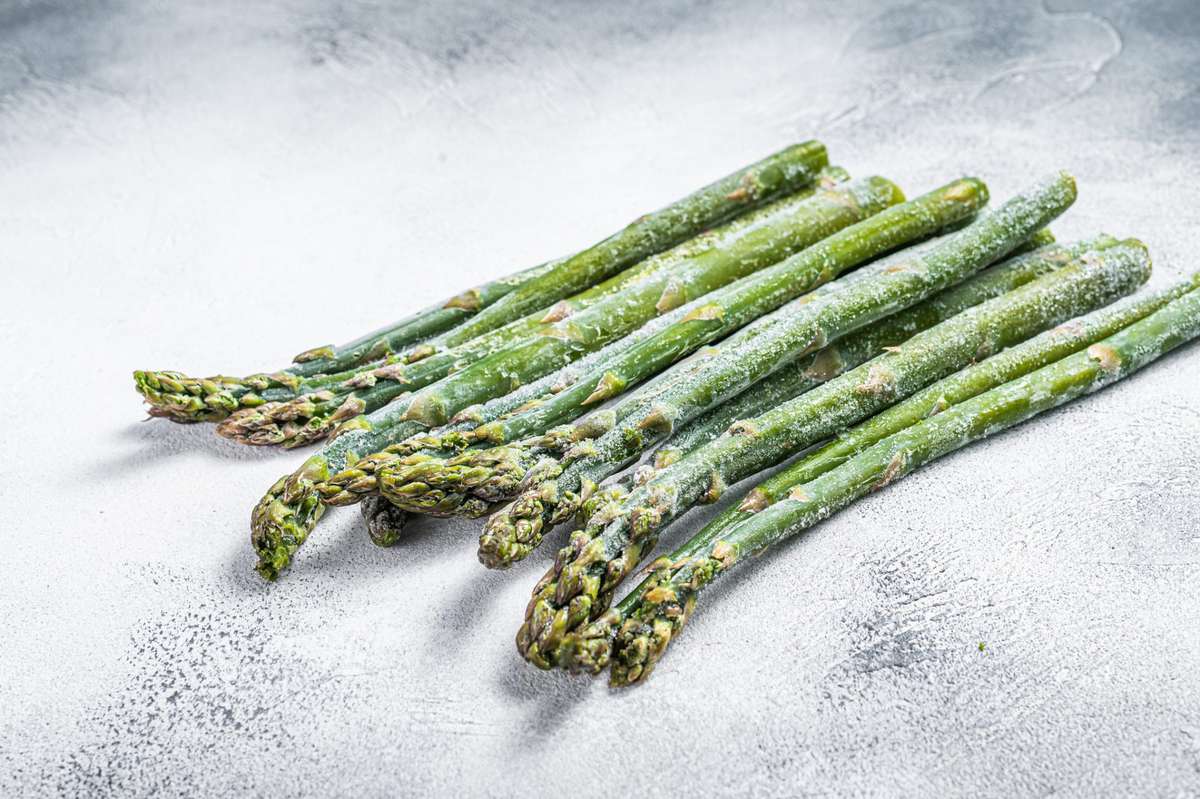 Frozen cold asparagus on a old kitchen table. White background. Top view