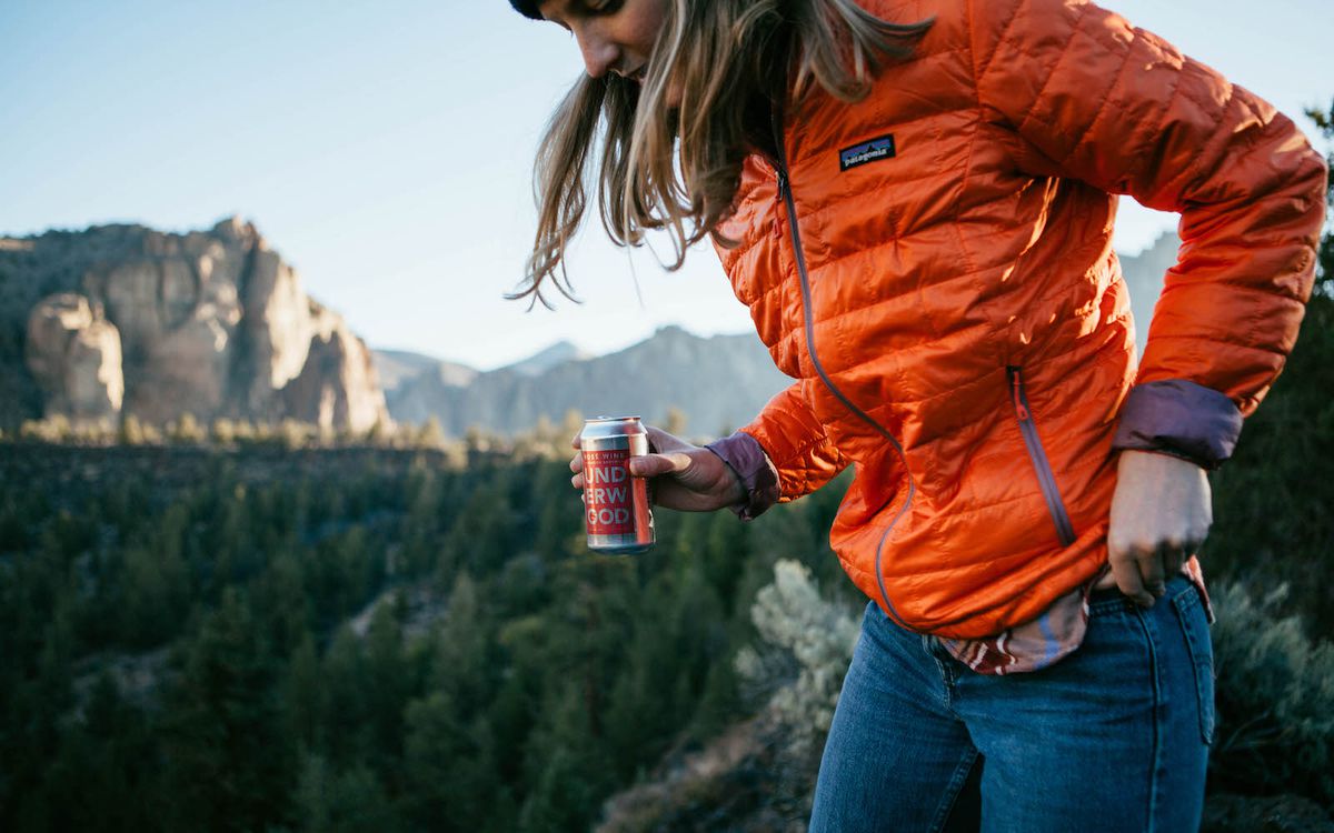 Woman climbs mountain holding wine in a can