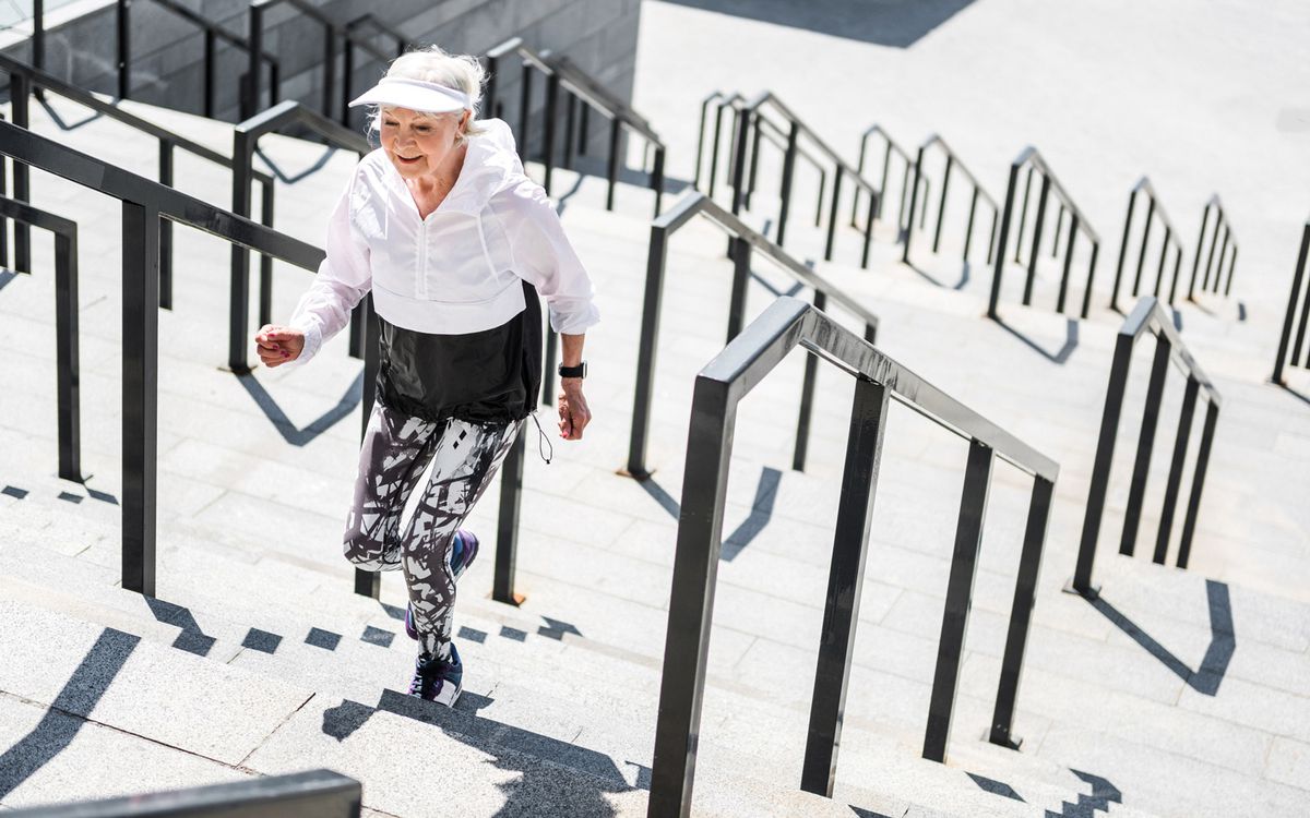 Happy old woman is climbing up city stairs outside. She is smiling and moving ahead. Copy space in right side