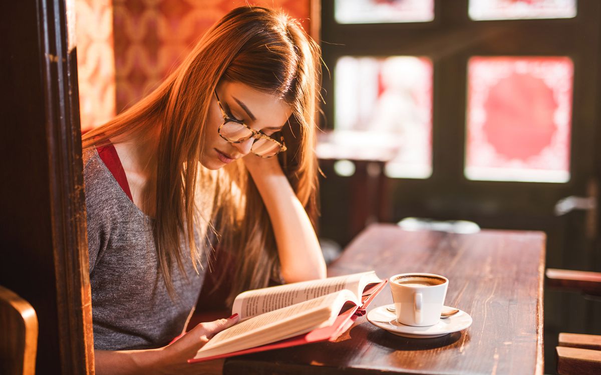 Young beautiful woman reading a book in a cafe