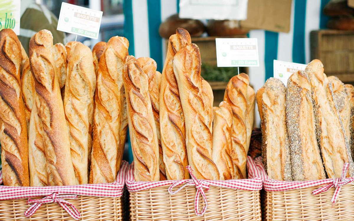 An assortment of freshly-baked baguettes on display in baskets at a farmer's market stall in Paris.