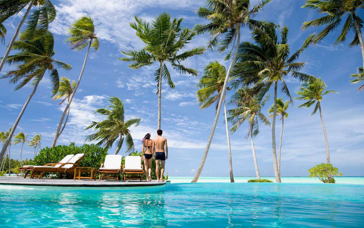 Couple walking past a resort pool, with palm trees