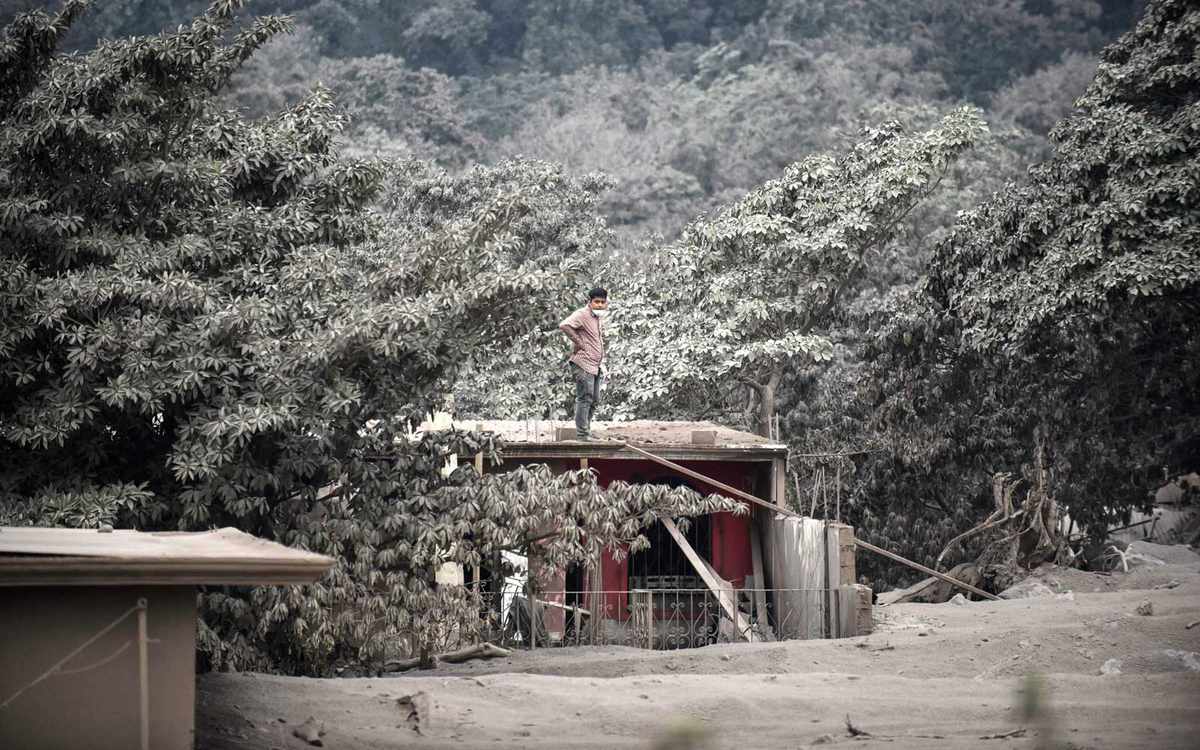 A man stands on the roof of a house in the ash-covered village of San Miguel Los Lotes, in Escuintla Department, about 35 km southwest of Guatemala City, taken on June 4, 2018, after the eruption of the Fuego Volcano.