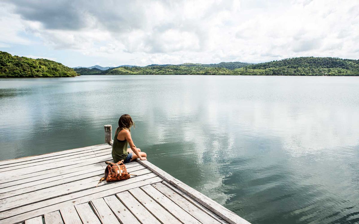 A woman sitting on a remote wooden dock overlooking a lake.