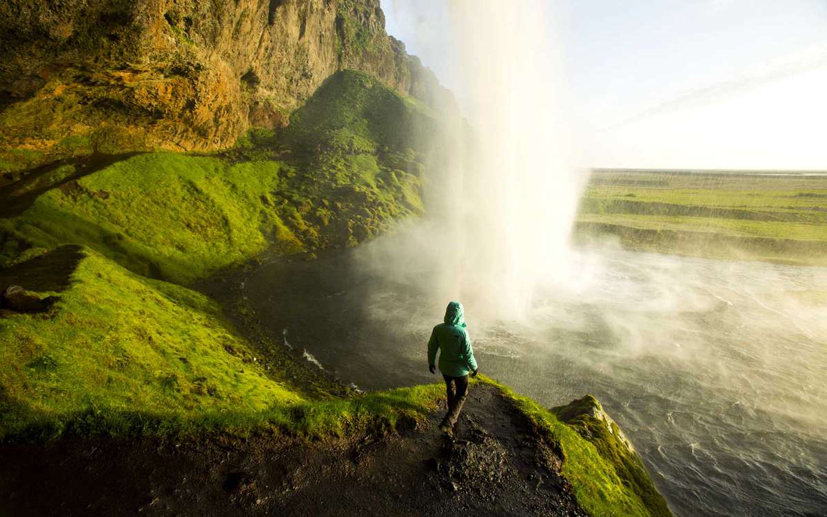 A woman watching the sunset from behind a waterfall in Iceland.