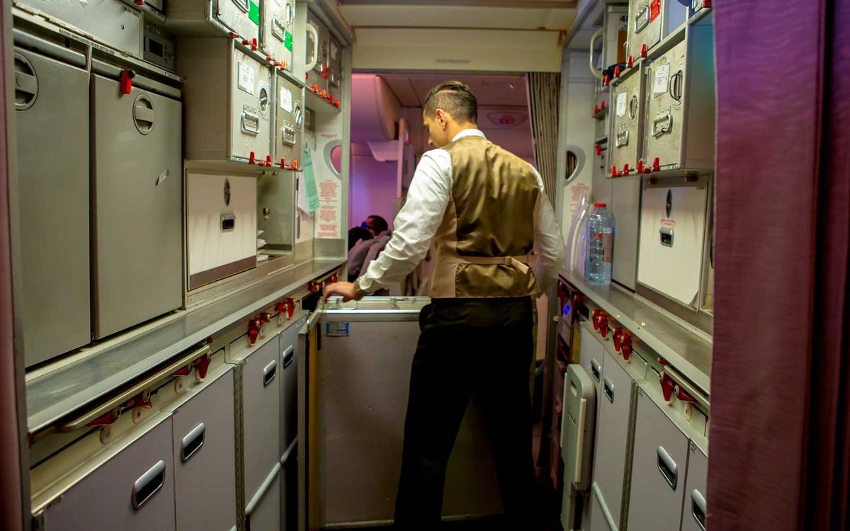 A cabin crew member moves carts in the galley.