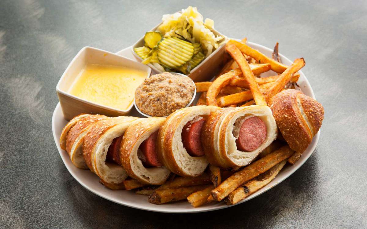 A kobe pretzel dog plate with fries, pickles and mustard dipping sauce