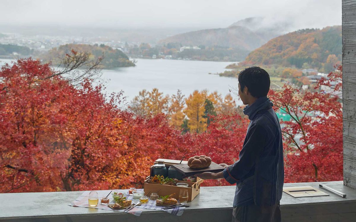 A man stands in front of fiery red autumn foliage from a terrace at the Hoshinoya Fuji resort