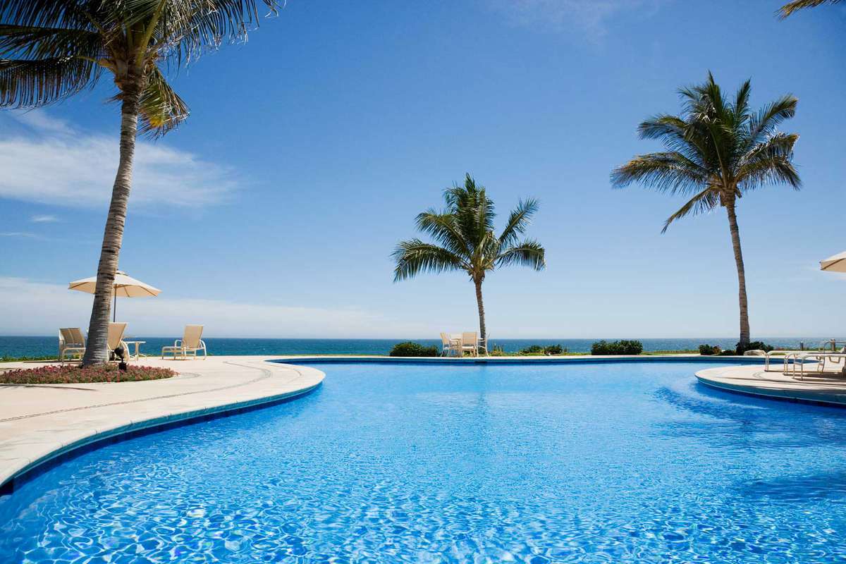 Vibrant blue water of a hotel pool surrounded by palm trees near the ocean