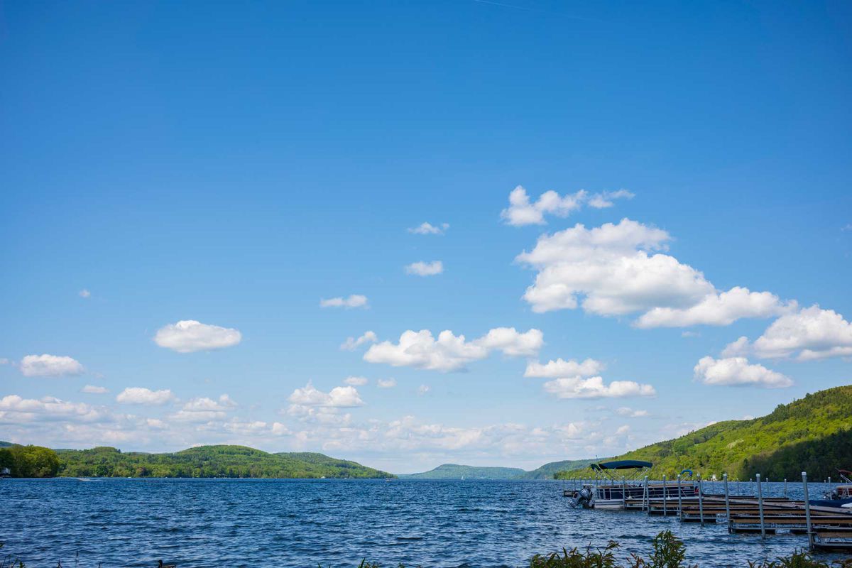The blue waters of Otsego Lake in Cooperstown, New York, on a sunny summer day with cumulus clouds in the sky, photographed near a dock.