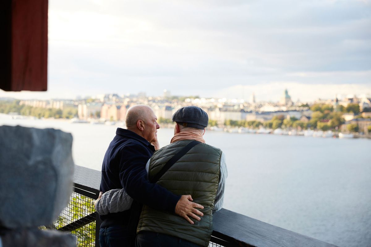 Gay couple embracing, looking out over river
