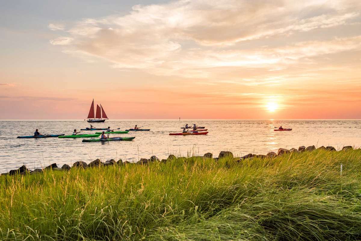 Kayakers and a sailboat offshore at Springer's Point on Ocracoke Island at sunset during summer.