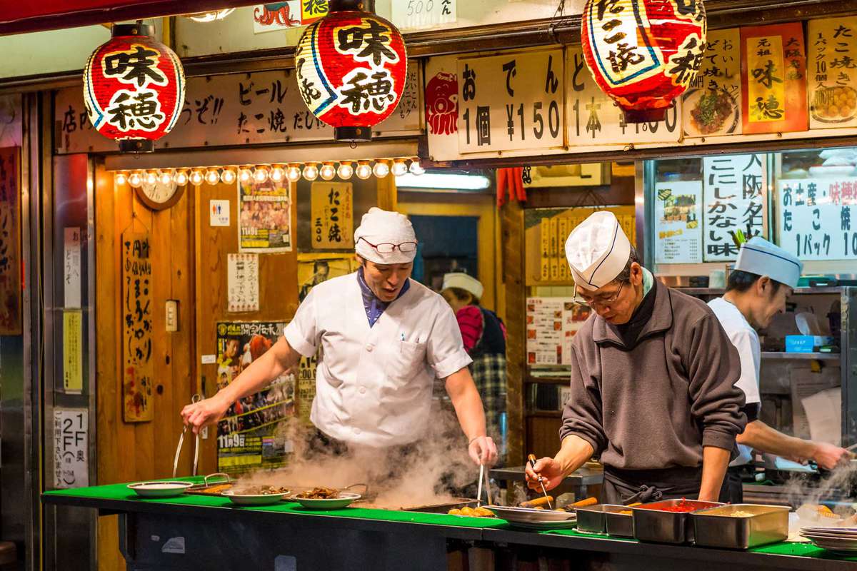 Homens cozinham comida de rua tradicional japonesa em Osaka, Japão.