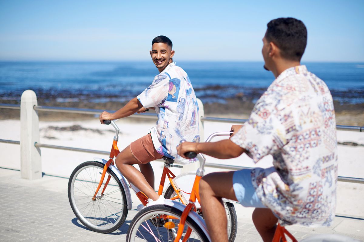 Young gay couple bonding together and riding bicycles along the promenade during a day out