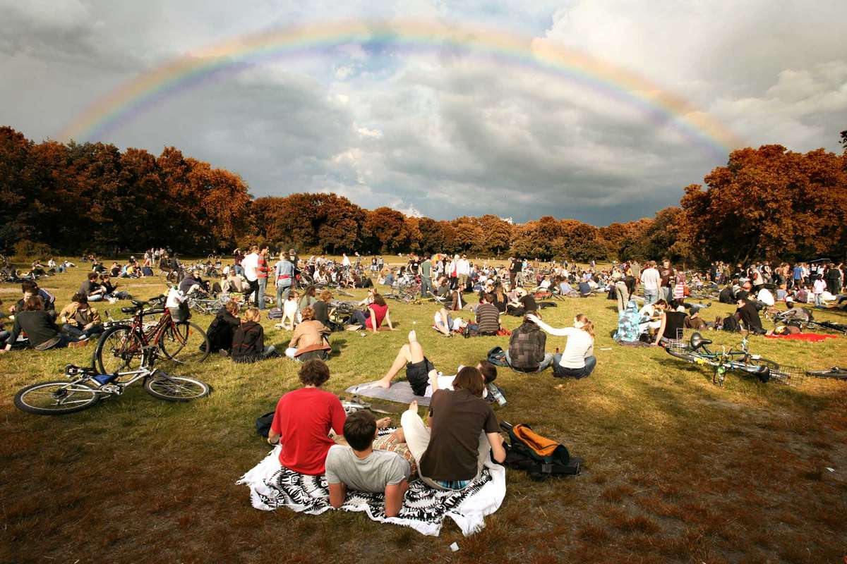 Young people laying down in grass and staring at rainbow over Hasenheide park in Berlin, Germany.