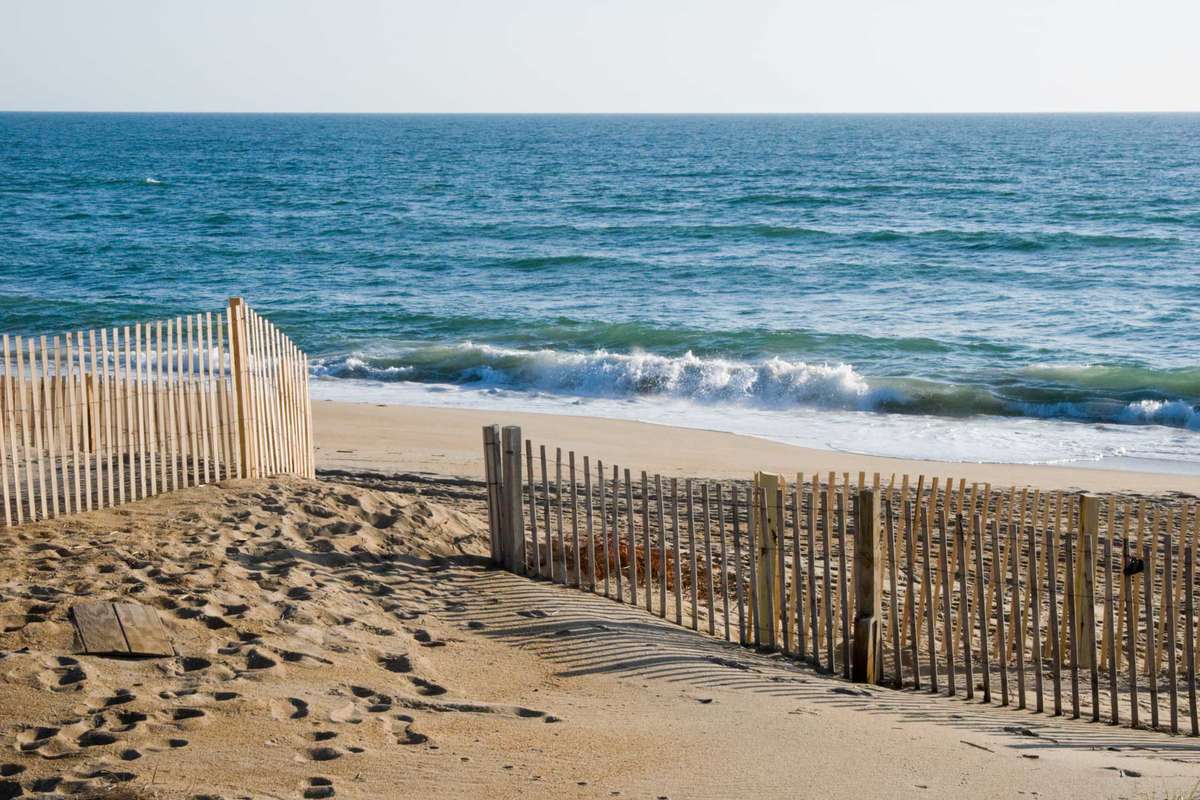 Waves breaking on the beach in morning light with an erosion control fence on the sand dunes, Outer Banks at Nags Head, North Carolina