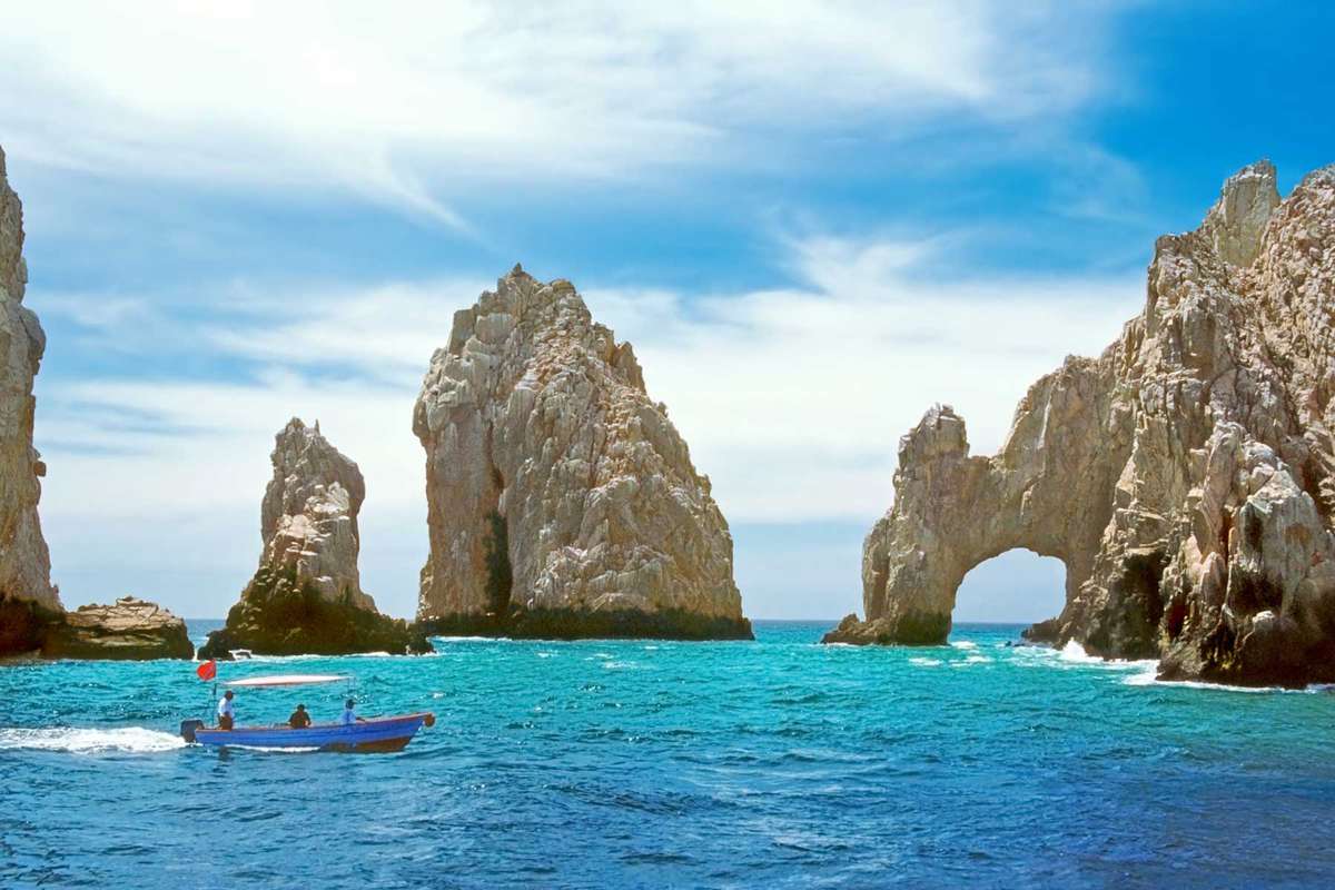 Inside the bay at Cabo San Lucas, a small tourboat is dwarfed by rock formations including the famous "El Arco."
