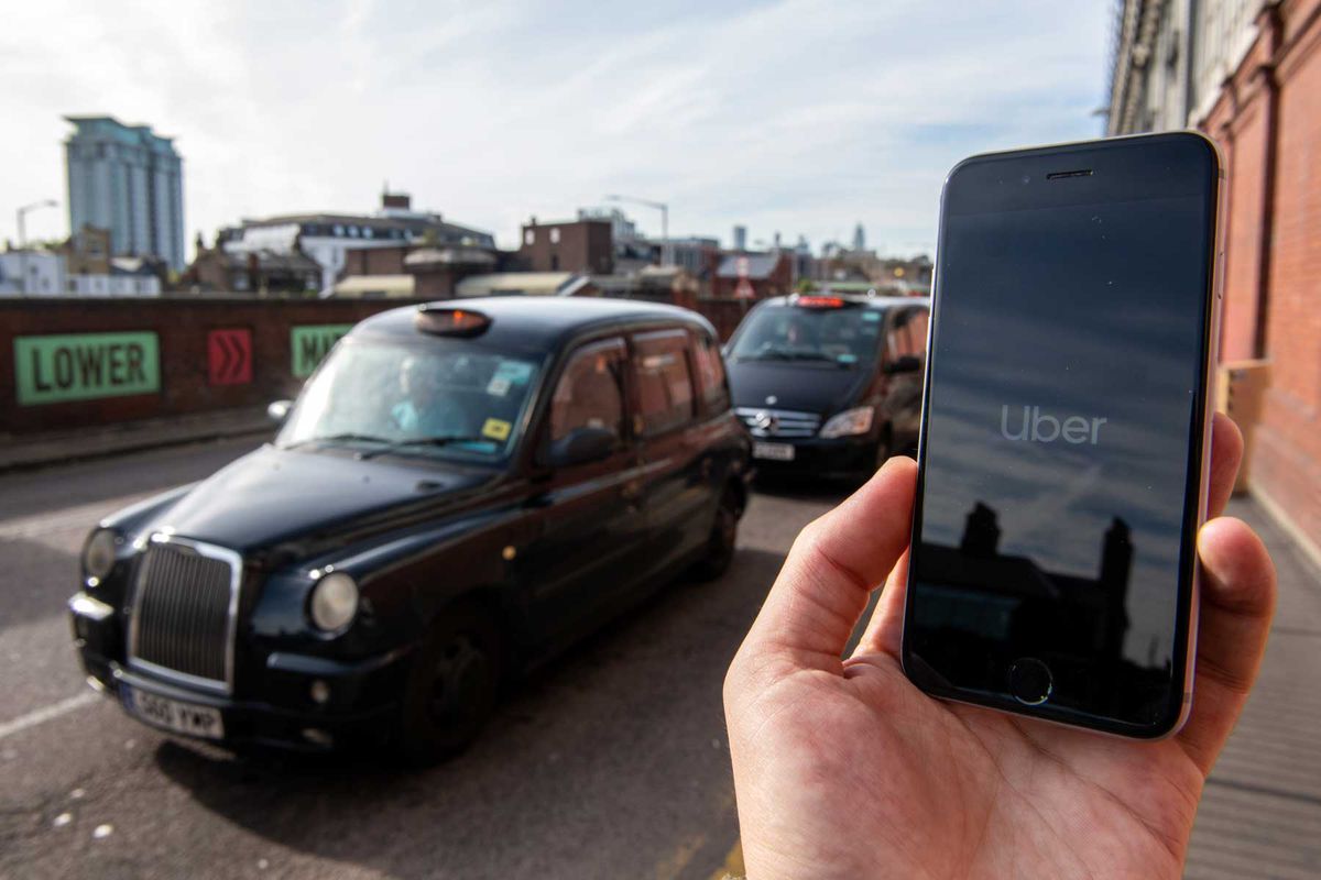 A phone is held displaying the Uber logo in its app in front of a taxi stand at Waterloo station on September 28, 2020 in London, England.