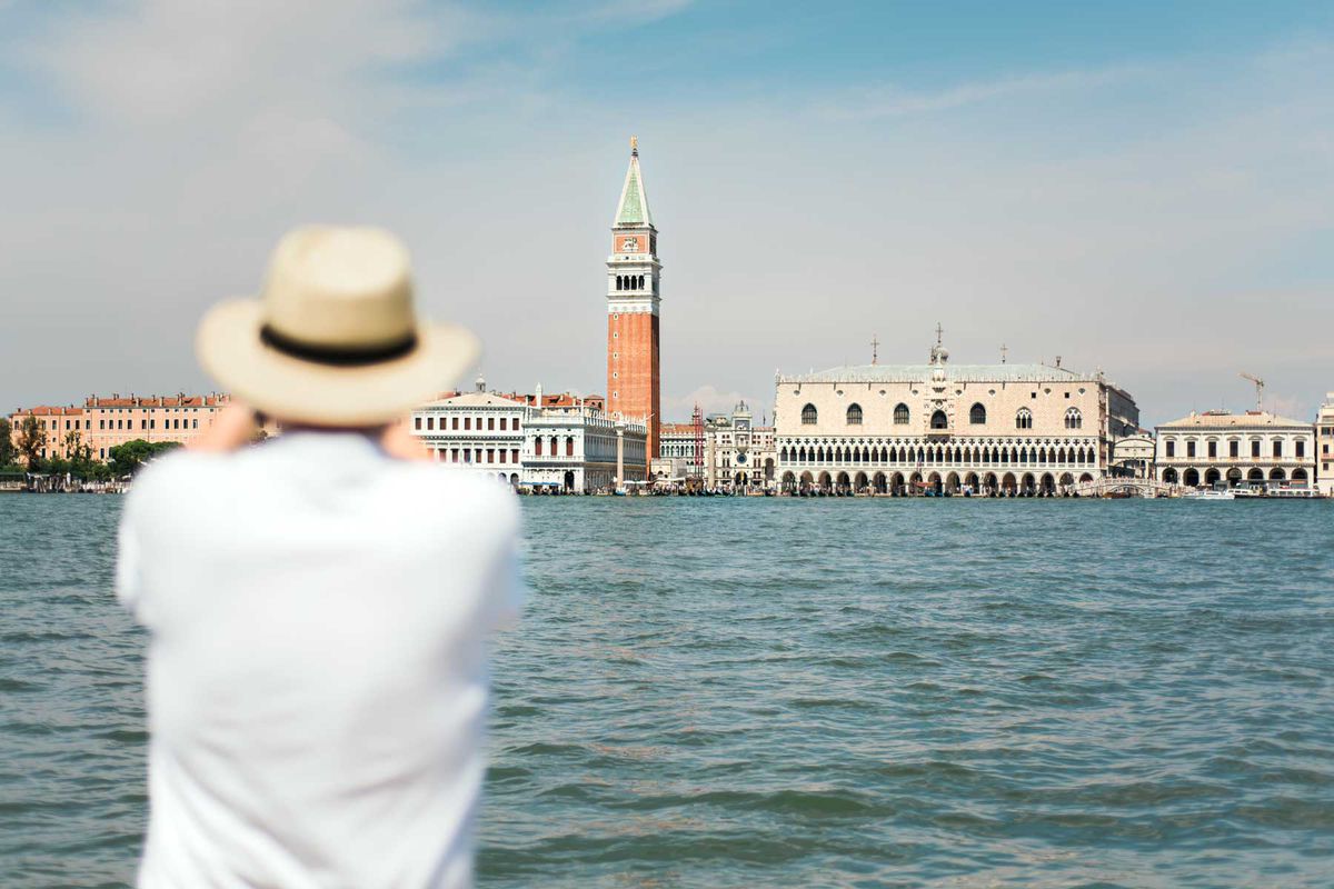View of a man taking a photo of the Campanile di San Marco and the Doge's palace, as seen from the Grand Canal, in Venice, Italy.