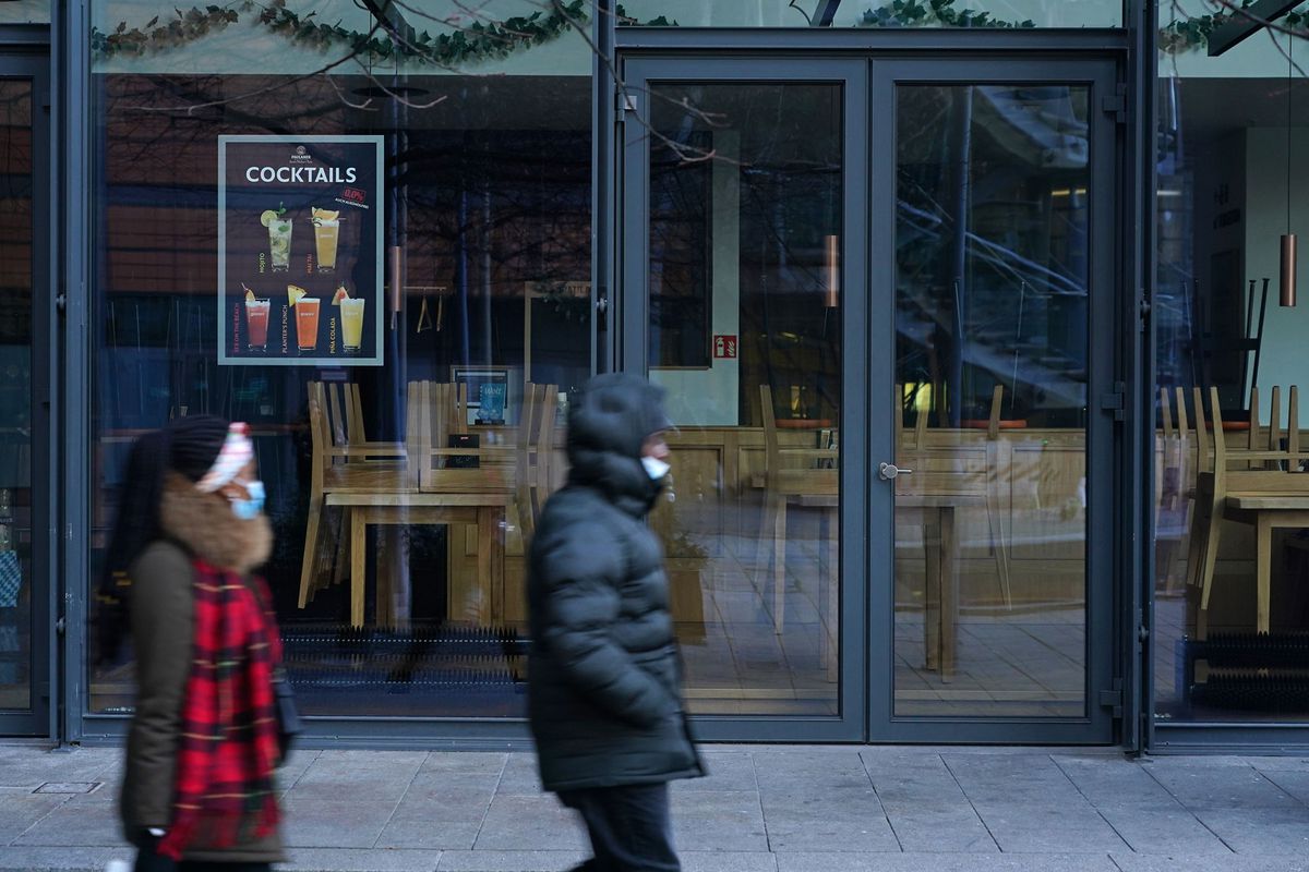 People wearing protective face masks walk past a shuttered beer pub