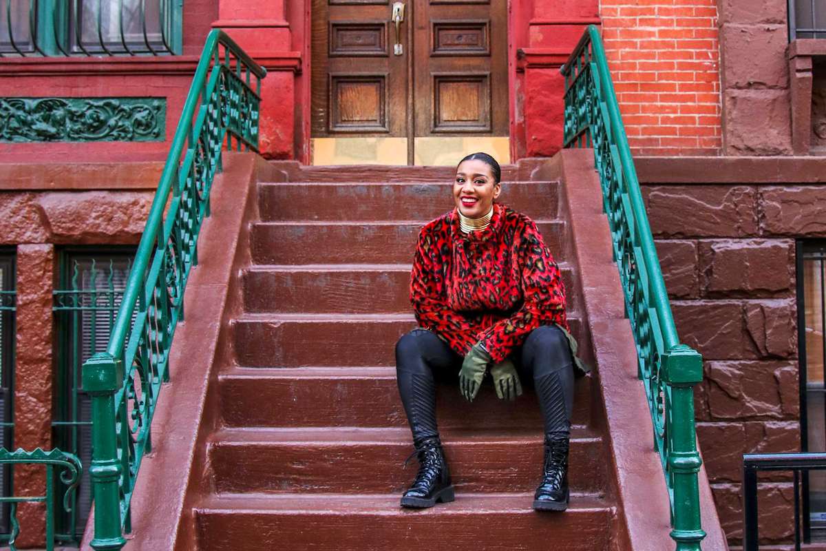 Evita Robinson sitting on the steps of a townhouse in Harlem, New York