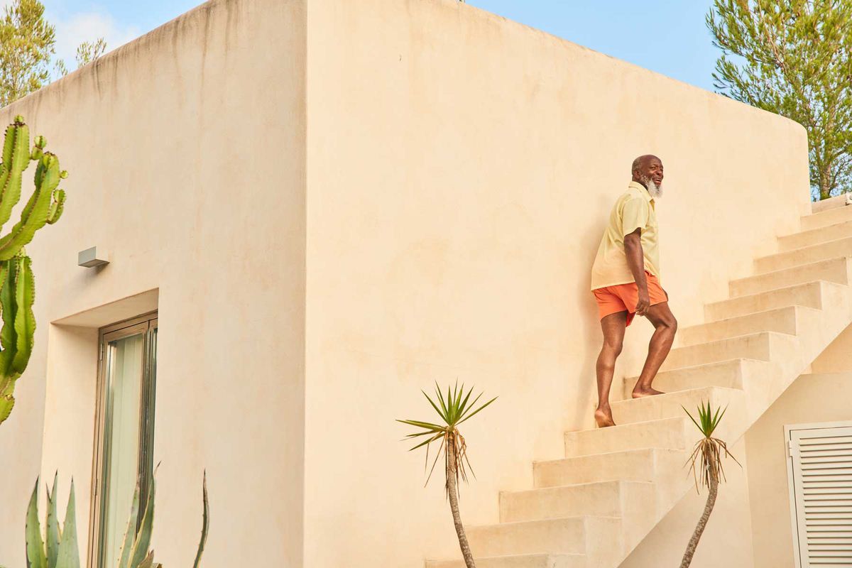 A man in a yellow shirt and orange shorts walks up stairs to a rooftop terrace while on vacation