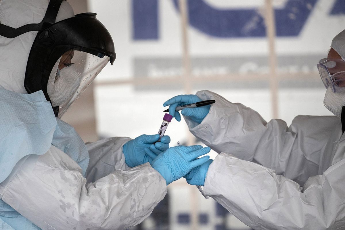 Health workers dressed in personal protective equipment handle a coronavirus test