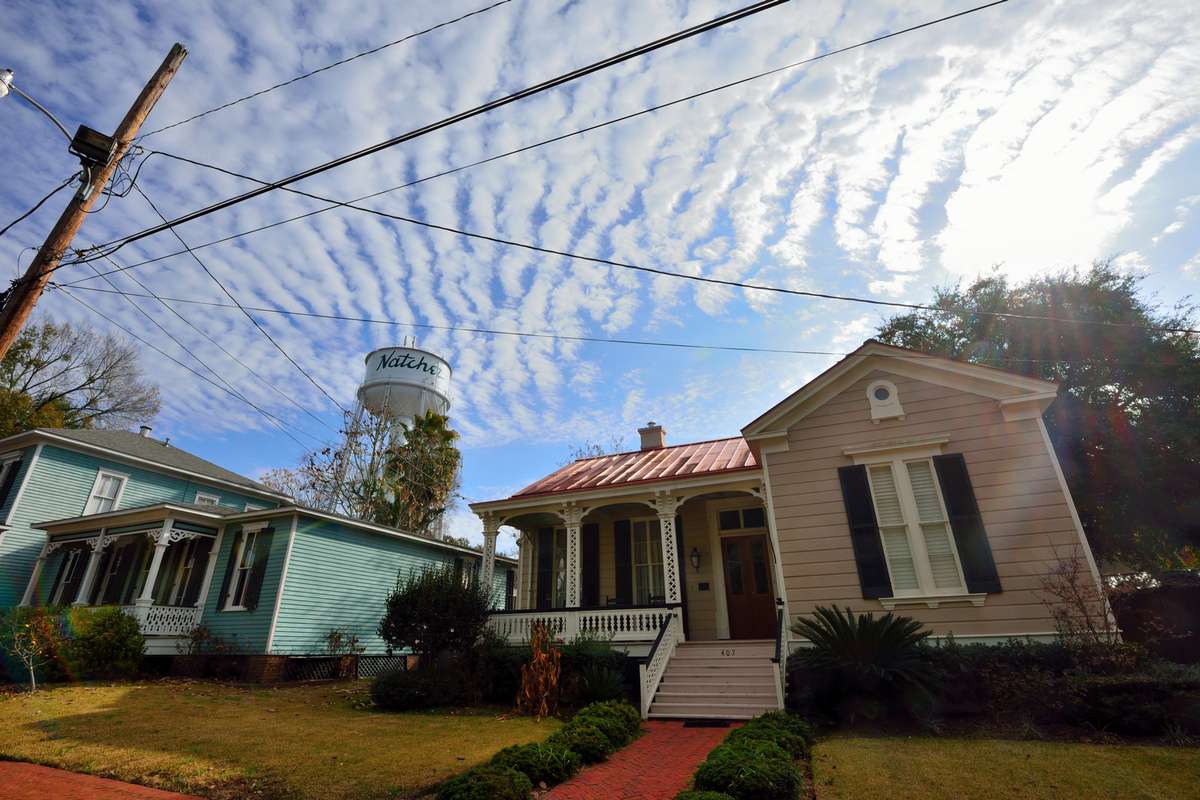 Two small wooden traditional American style houses with watertower in the background against a mackrel cloud sky in Natchez, Mississippi