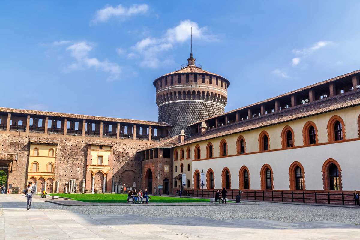 Old medieval Sforza Castle Castello Sforzesco, green lawn of courtyard, blue sky white clouds background.