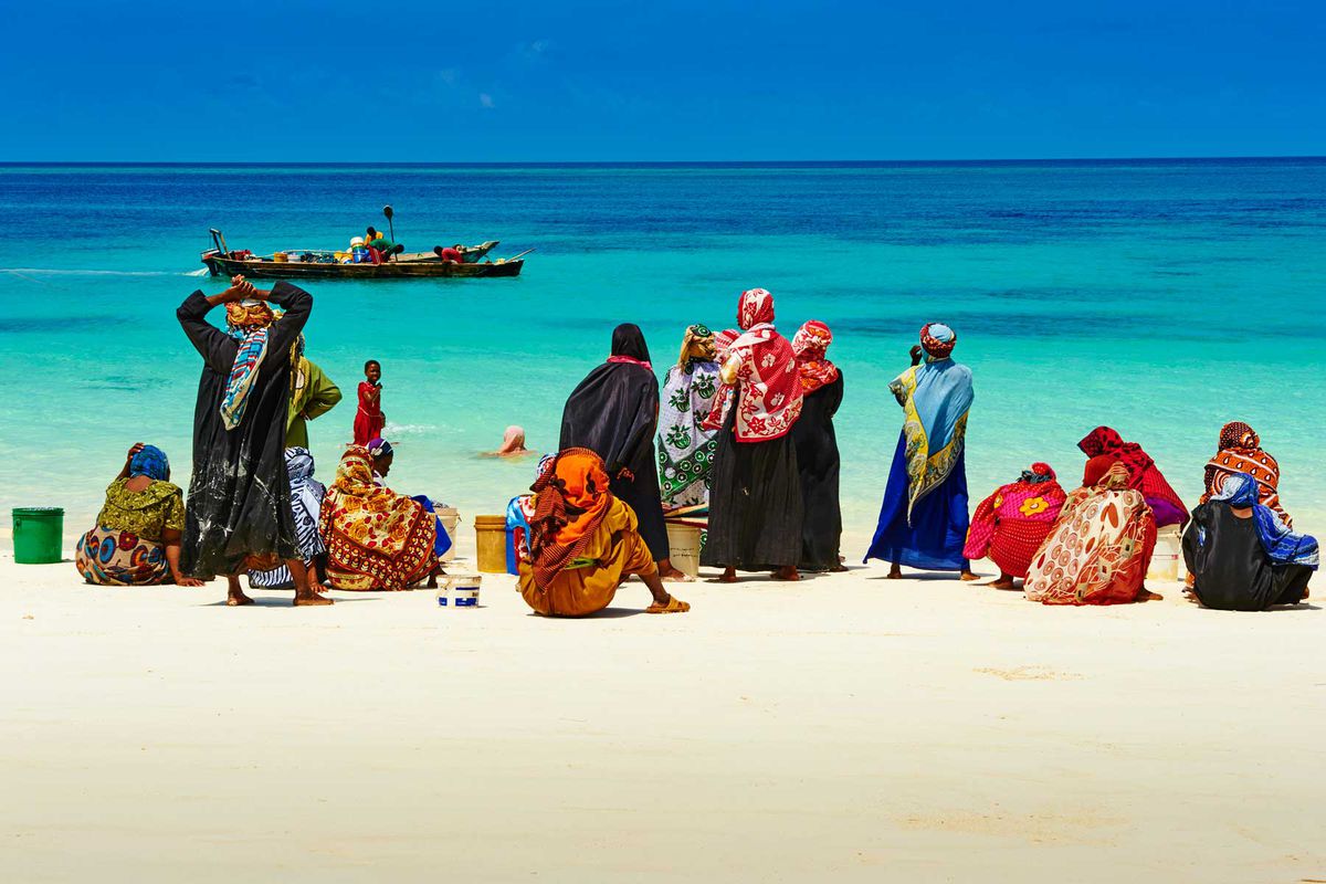 Women lined with a fishing boat in the distance on the Nungwi beach in Unguja, Zanzibar Island in Tanzania. Tanzania