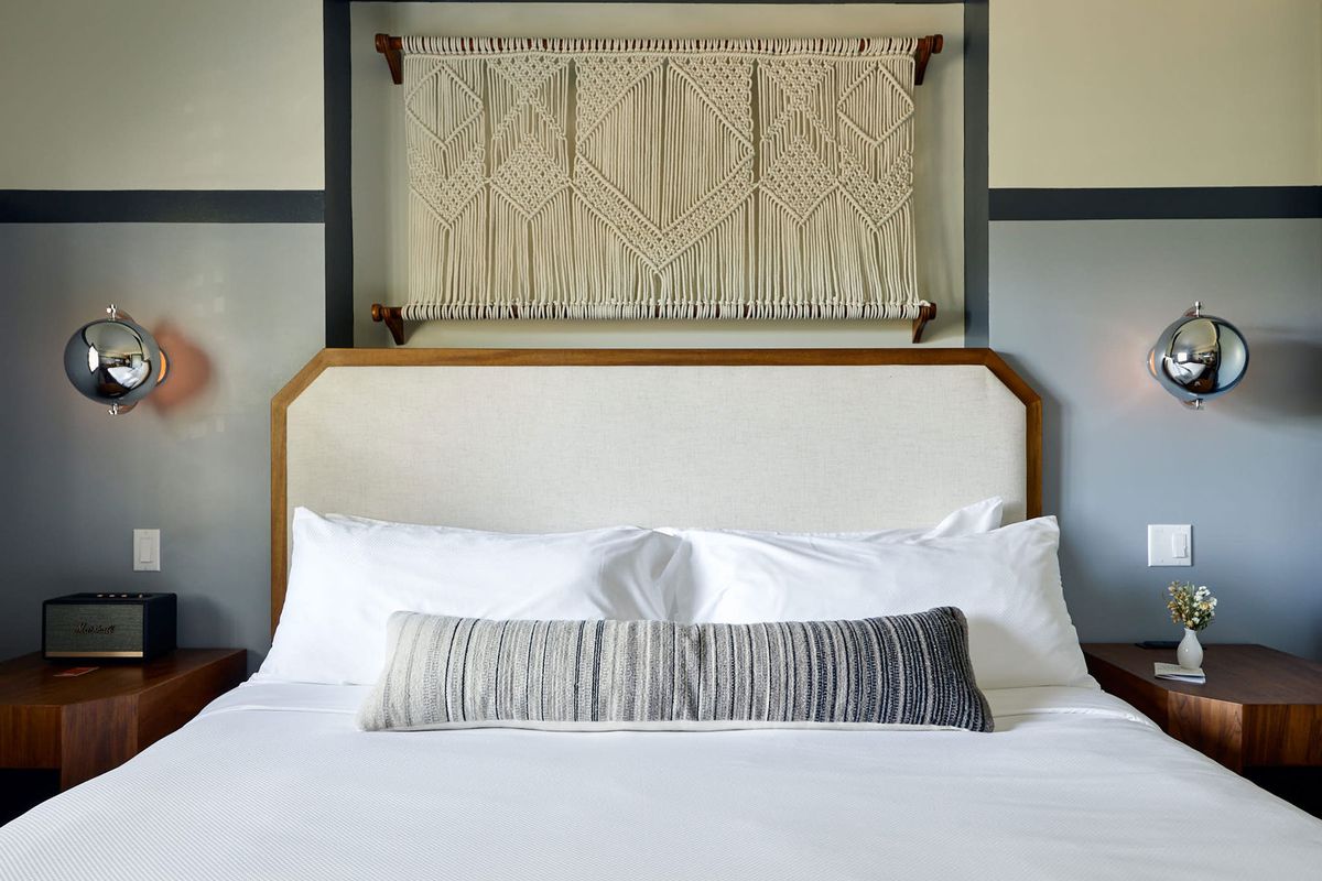 large bed with white sheets below rope wall hanging