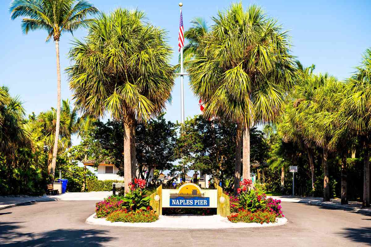 Naples pier, Florida entrance sign with palm trees and American flag on flagpole in wealthy neighborhood community