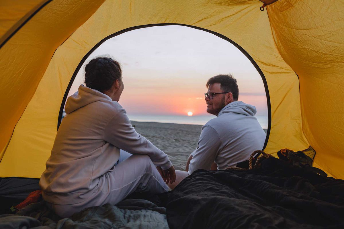 A couple sitting in camping tent looking at sunset.