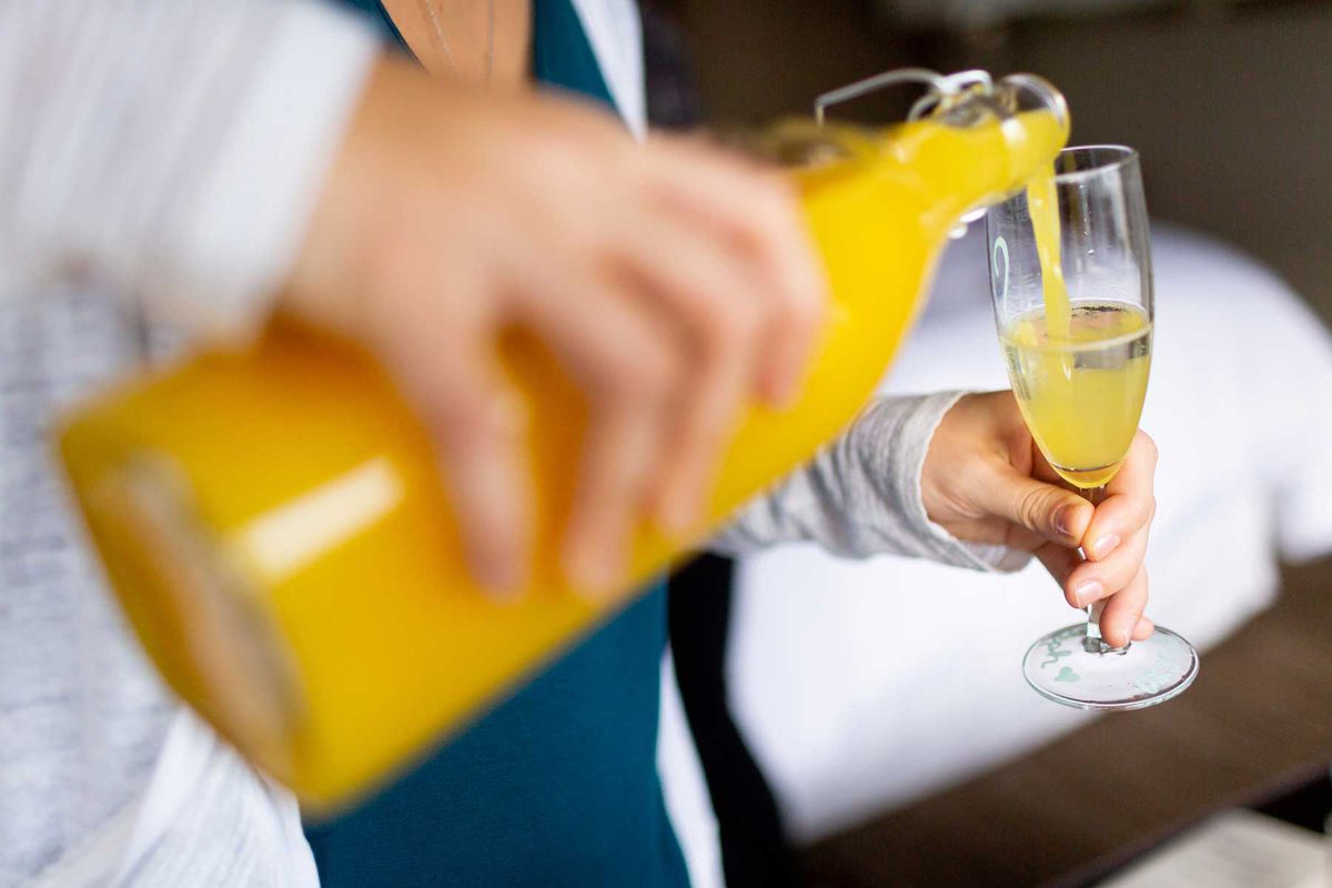 Woman pouring orange juice into champagne in glass to make mimosa
