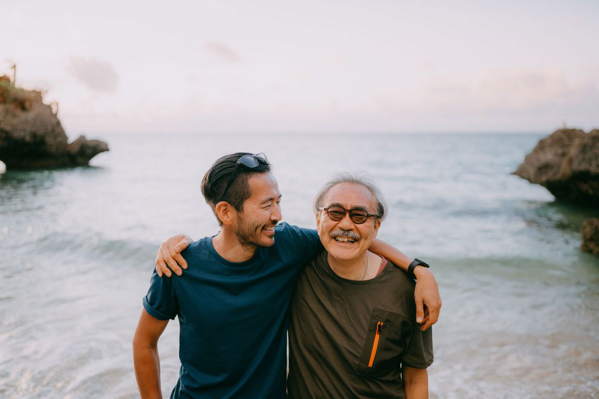 Japanese senior father and adult son having a good time on beach at sunset